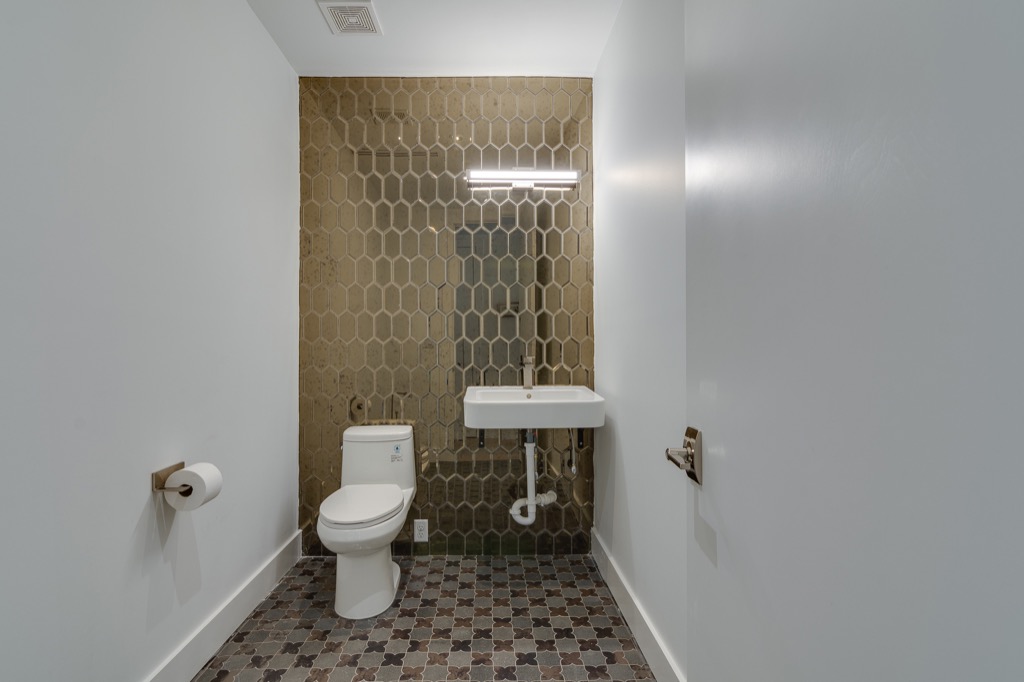 A restroom with a brass hexagon tile wall and a patterned tile floor