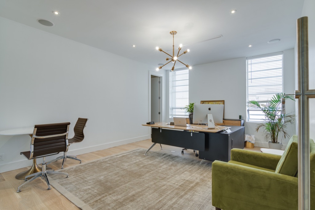 A furnished private office with a desk, lounge chairs and a green velvet sofa