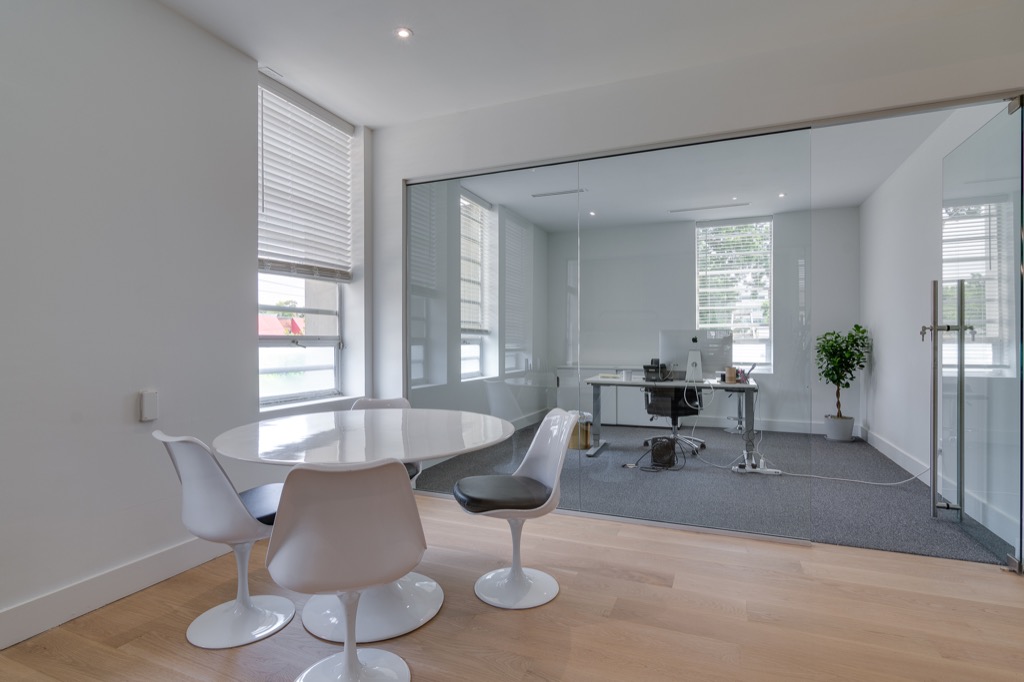 A room with a round table and chairs beside a glass office wall